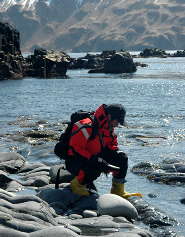 a NOAA scientist checks an Alaskan shoreline for oil beached after a 2004 oil spill.